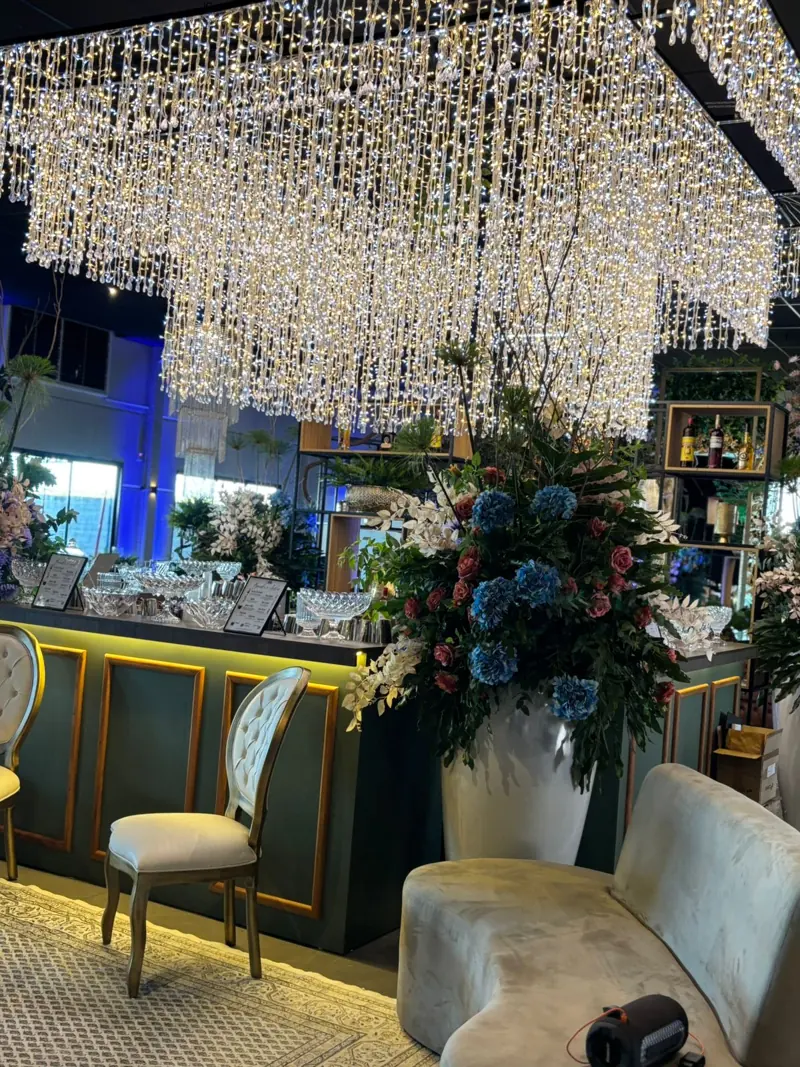Bar do salão com arranjo de hortênsias e rosas sob cortina de luzes