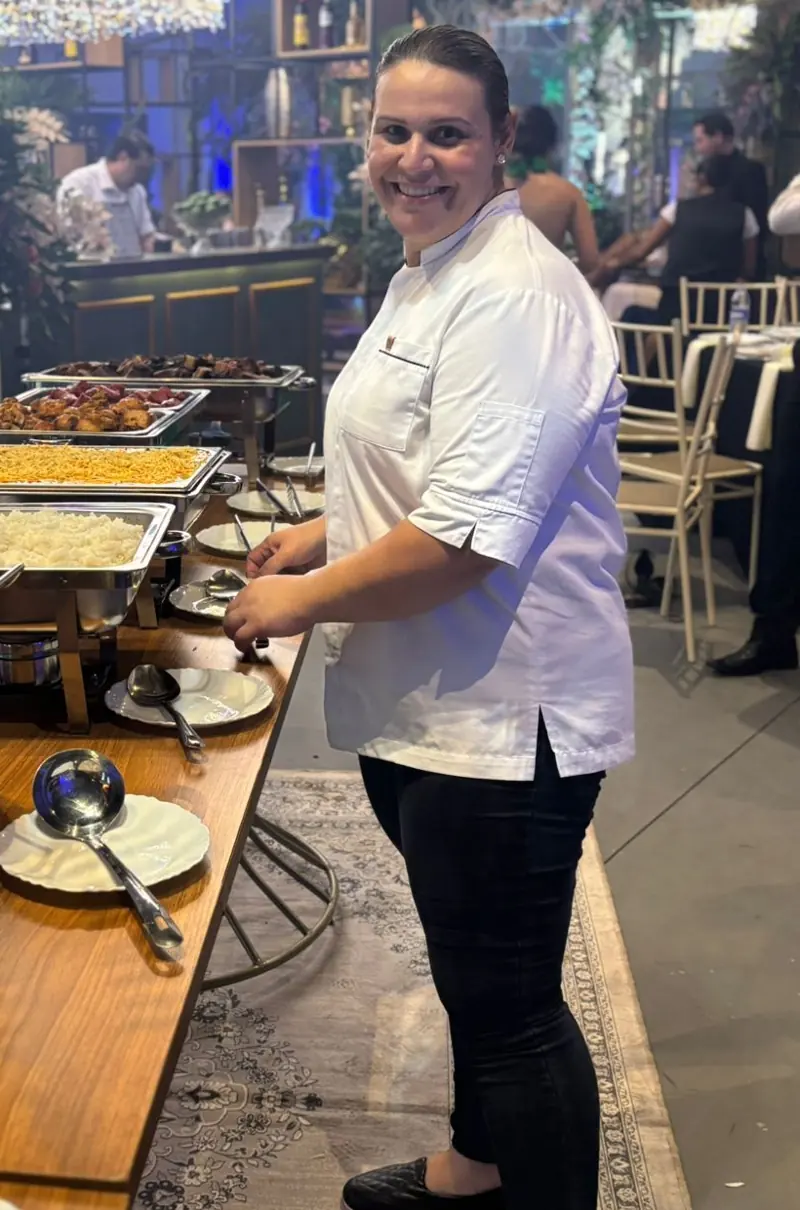 Brígida Leila sorrindo ao lado do buffet montado num salão de festa